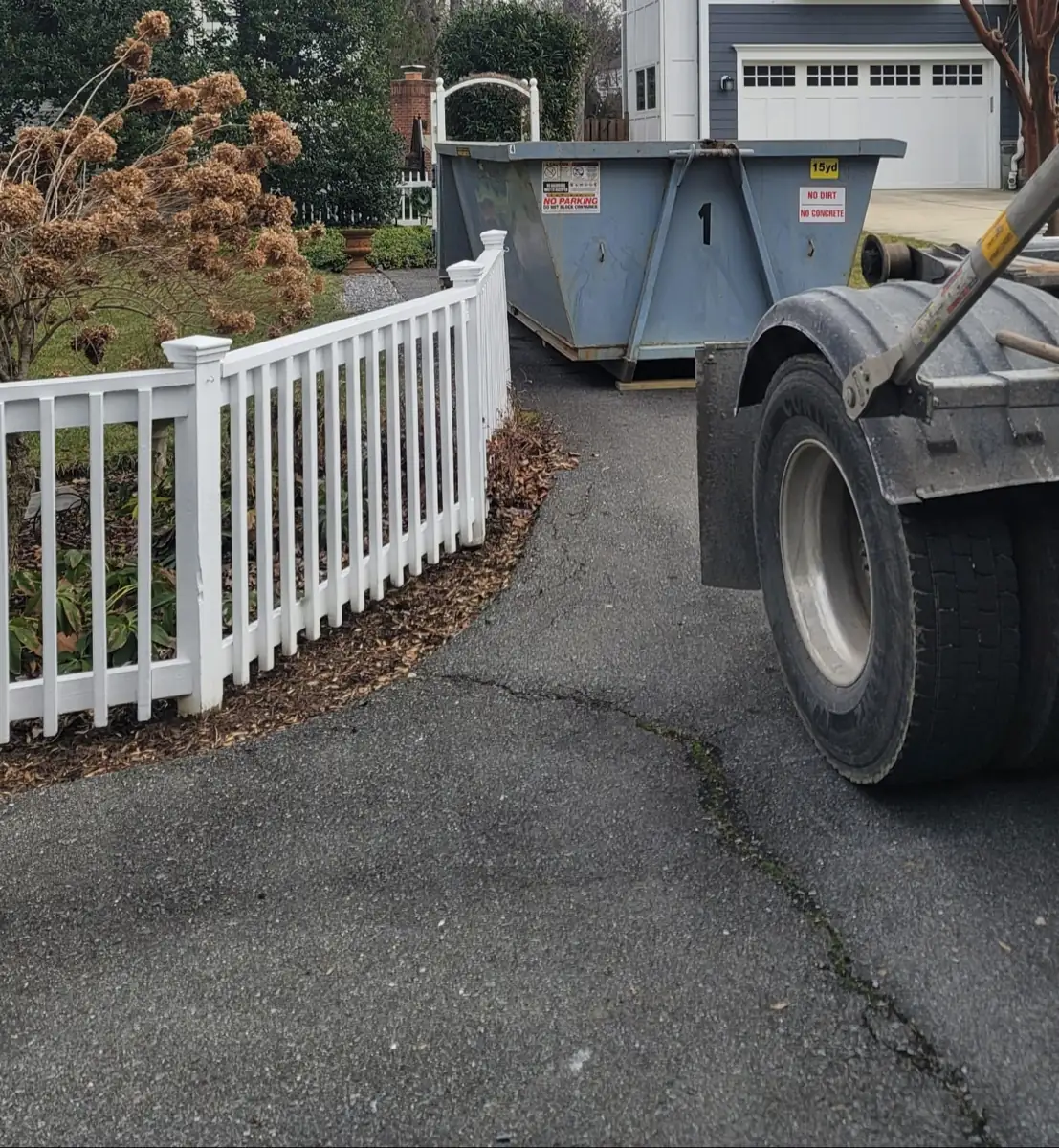 Roll Off On The Go truck backing a container up a curved driveway past a white picket fence in Bethesda, MD