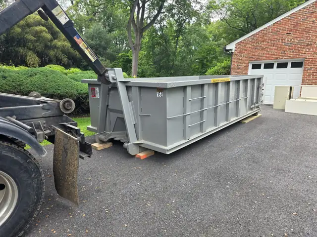 Truck setting a roll off container on wood boards in a driveway beside a brick garage in Potomac, MD