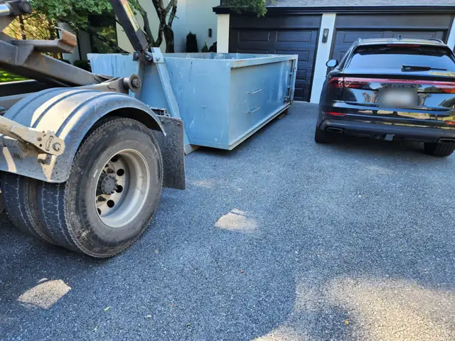 Roll off container being placed on a dark gravel driveway in Potomac, MD