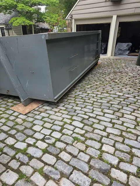 Roll off container on boards over a cobblestone driveway in Rockville, MD