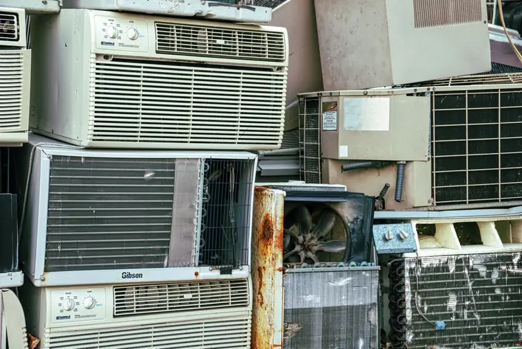 Pile of old window air conditioners and worn appliances stacked on top of each other