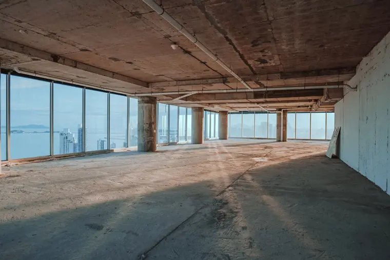 Empty office floor stripped to bare concrete with floor-to-ceiling windows along one side
