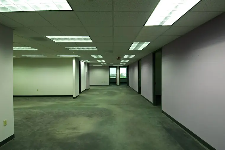 Long vacant office corridor with carpet, drop ceiling lights and empty rooms on both sides