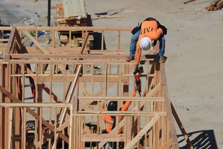 Two framers in hard hats and orange shirts working on top of a wood wall frame