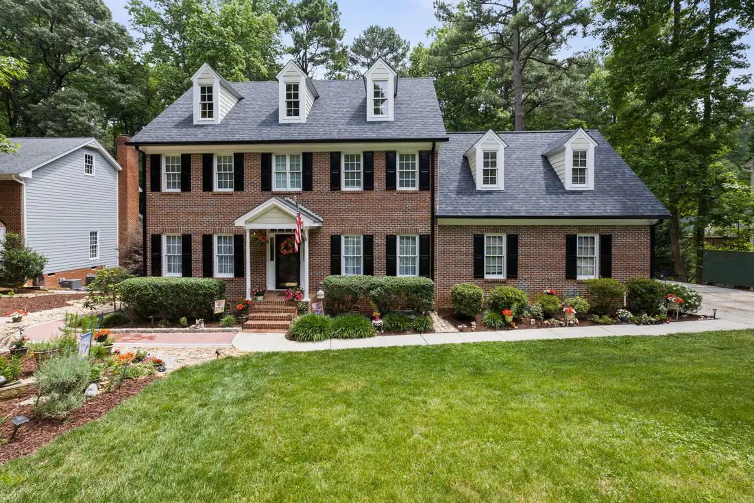 Two-story brick colonial with black shutters, dormers and a landscaped front lawn