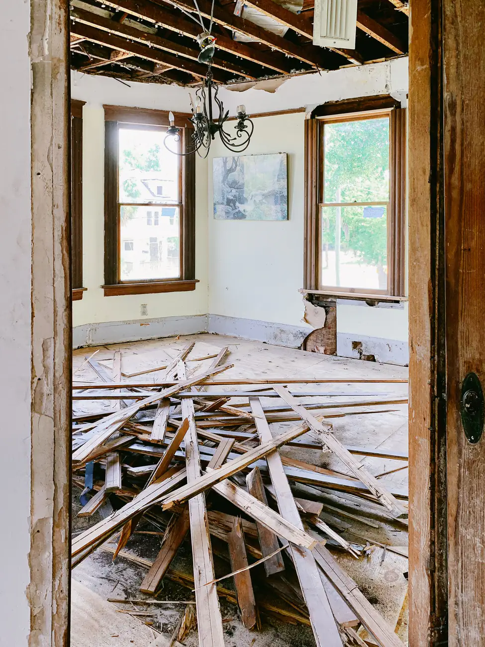 Doorway view into a gutted room with old floorboards torn up and piled in the middle of the floor
