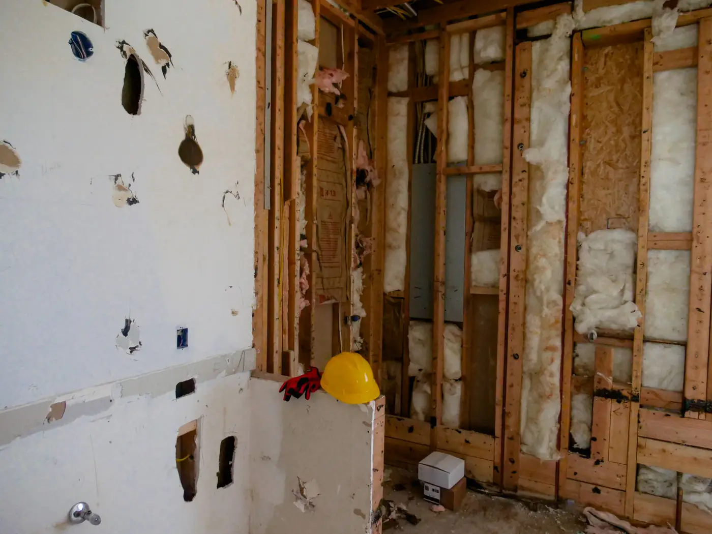 Interior walls opened up to the studs during a remodel, showing insulation, patched drywall and a yellow hard hat
