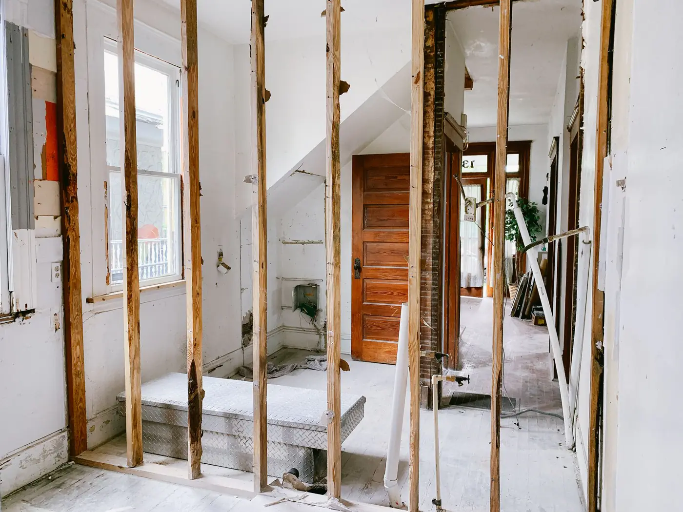 Hallway of an older house gutted down to bare wood studs, with an original wood door in the background